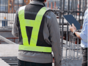 Arbeider i refleksvest på byggeplass ser på et nettbrett med tilgang til CAD-filer.